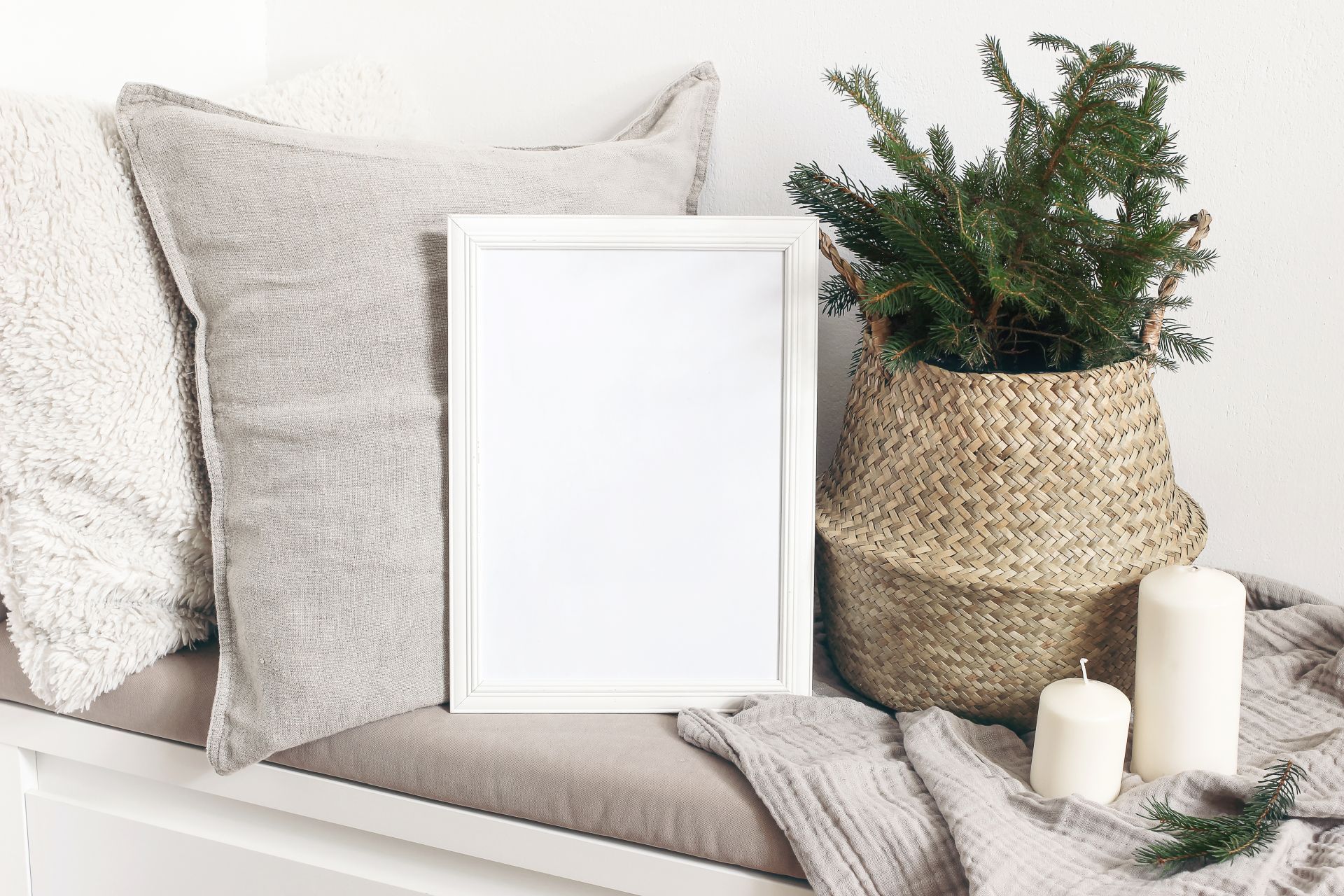 White blank wooden frame mockup with Christmas tree, candles, linen cushions and plaid on the white bench. Poster product design. Scandinavian home decor, nordic design,inter festive concept.